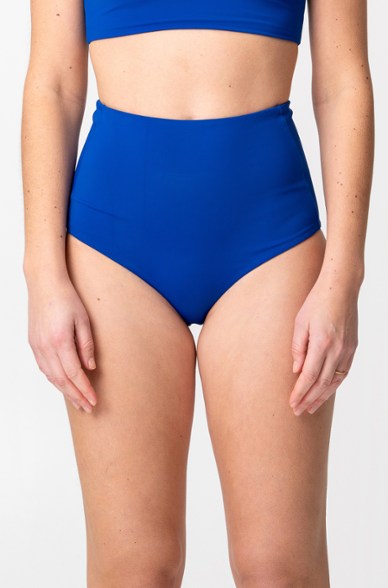 Model standing poolside wearing high waisted bikini bottoms in slate blue