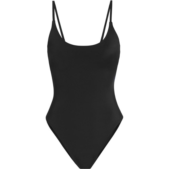 Woman confidently posing in a sleek black Serenity scoop neck one-piece swimsuit with bust support at the beach, showcasing its flattering fit.