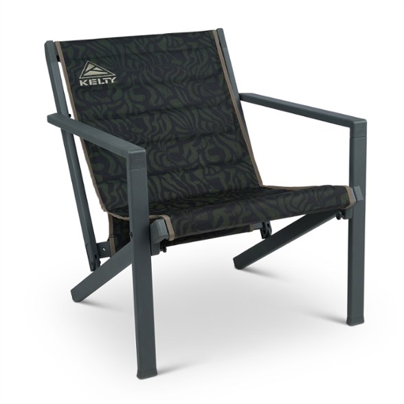 A person comfortably lounging in the Trailblazer Elite Folding Camp Chair, set up at a scenic campsite with trees in the background, showcasing its portable design.