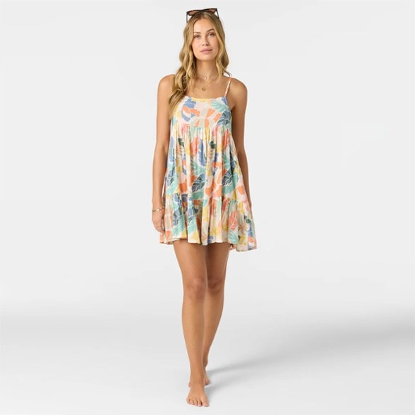 Woman smiling and walking on a sandy beach wearing the colorful tiered Island Bloom beach dress with adjustable straps.