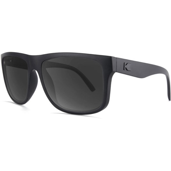 A man wearing OceanVue MaxFit polarized sunglasses with green lenses, hiking a sunny mountain trail, showcasing their wide fit and UV protection.