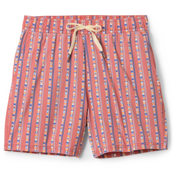 Model wearing Tropics 5-Inch Retro Recycled Swim Trunks in a sun-faded blue, standing on a beach with ocean in background, showcasing the classic fit.