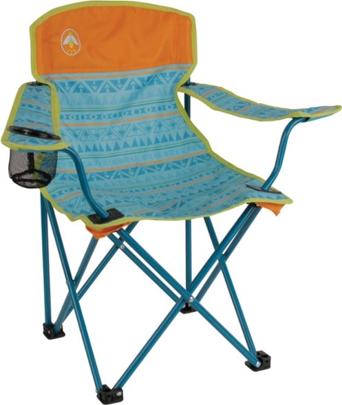 A child happily sitting in a glow-in-the-dark Coleman kids camping chair at a campsite, with trees in the background.