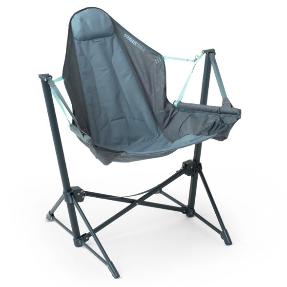 A person comfortably lounging in the Stargazer Pro reclining chair at a campsite, showcasing its auto-recline feature and integrated cup holder.