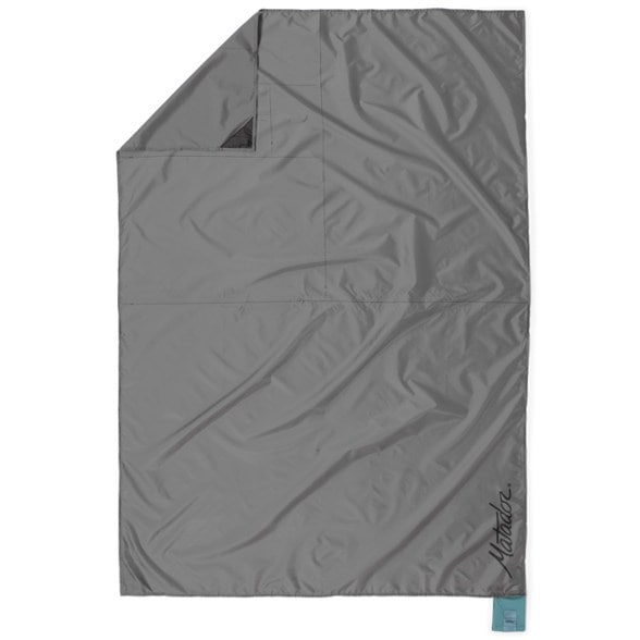 Waterproof pocket blanket unfolded on grassy terrain during a camping trip