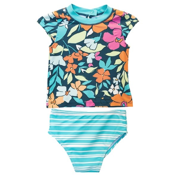A happy toddler girl wearing a pink and blue floral rash guard for toddlers and matching swim bottoms, playing in the sand at the beach.
