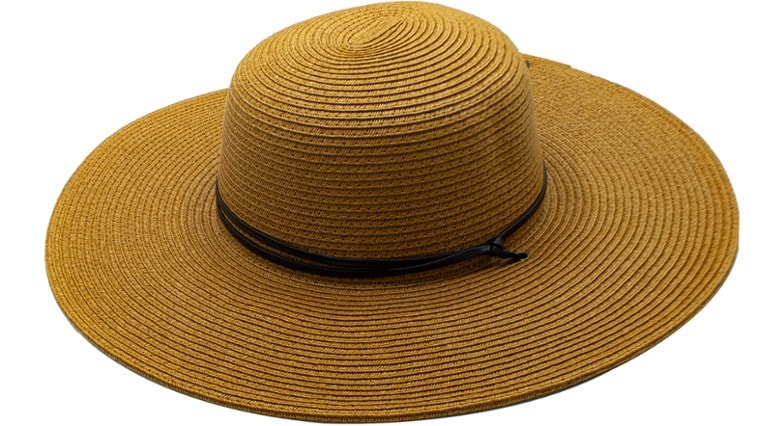 A woman wearing a wide-brimmed UPF 50+ sun hat, facing the sun, highlighting the hat's protective design for beach use.